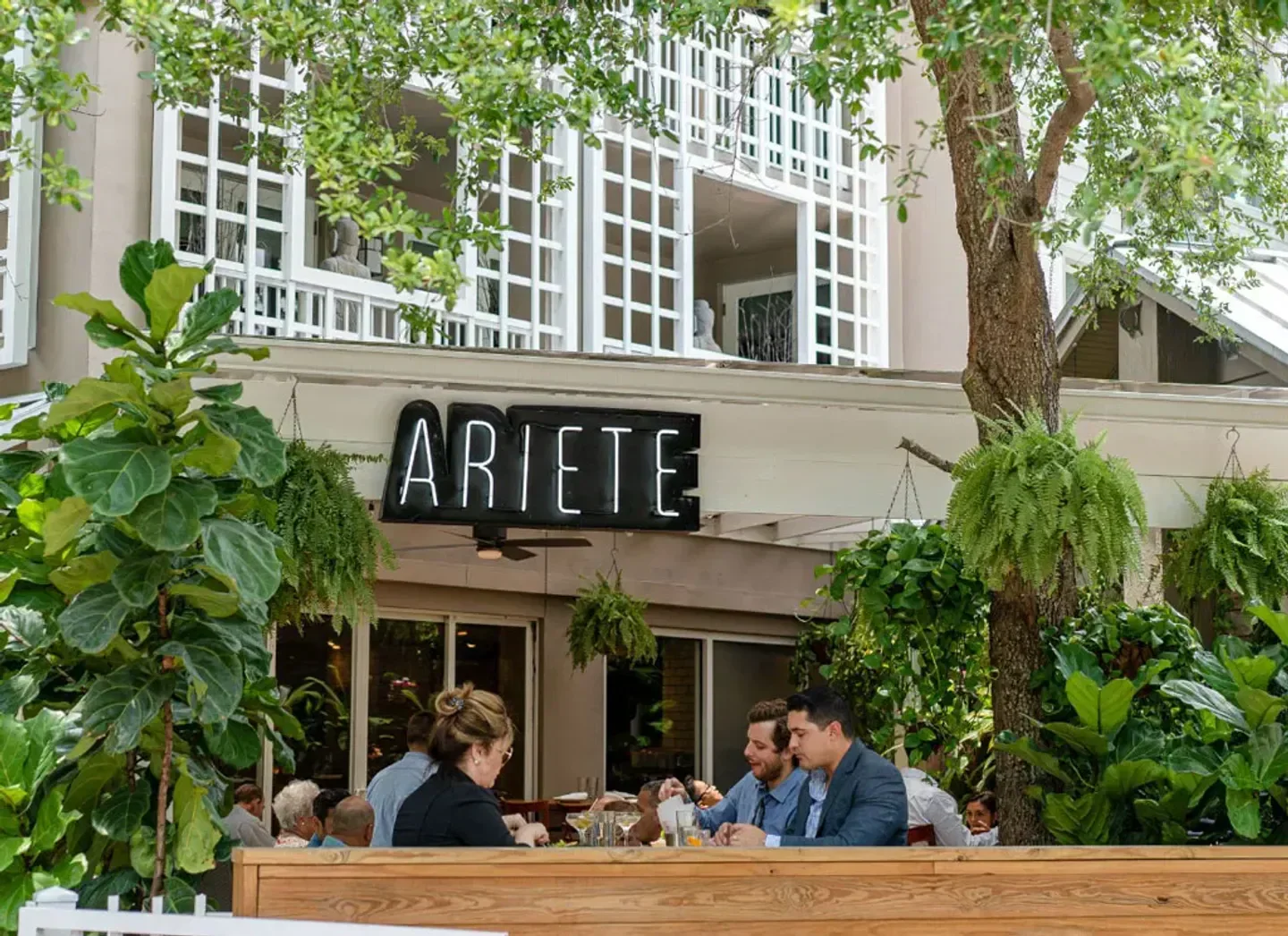 Outdoor dining scene at Ariete restaurant in Miami with lush greenery and patrons.