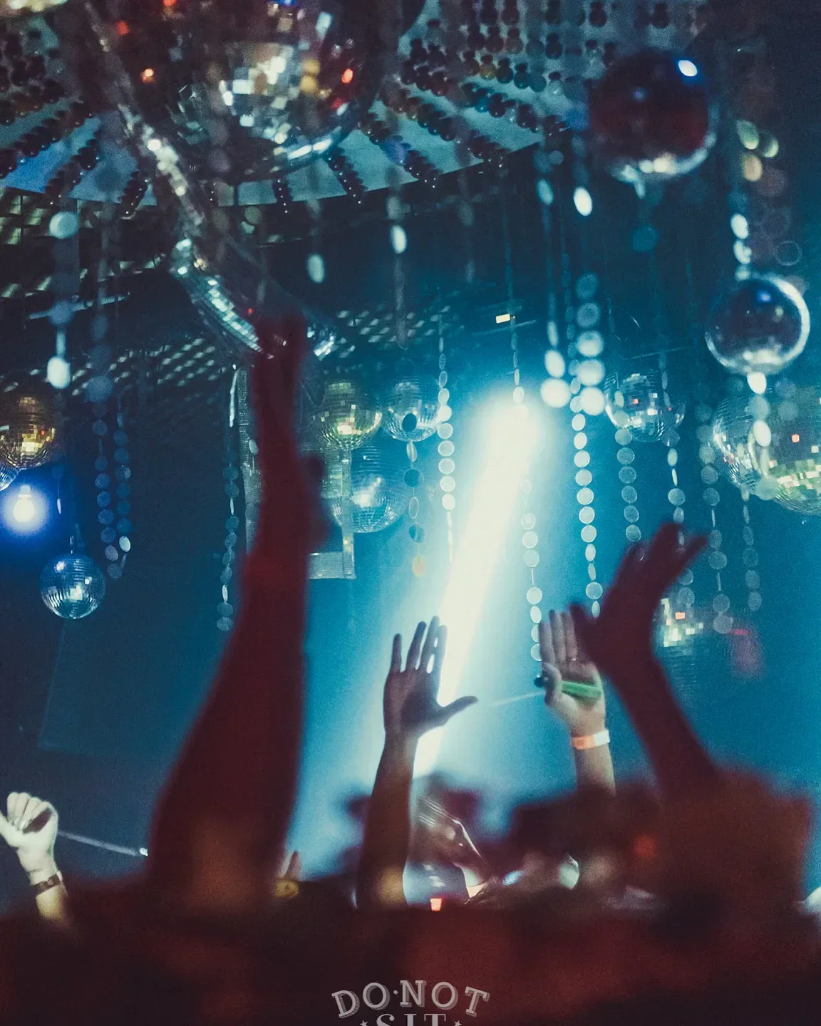 Dancing crowd at Do Not Sit nightclub in Miami, surrounded by disco balls.