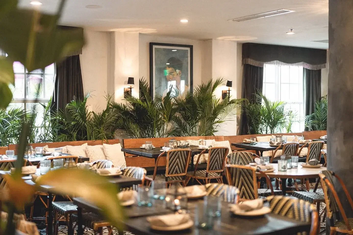 Gitano Miami restaurant interior, featuring tables, chairs, plants and a vintage artwork.