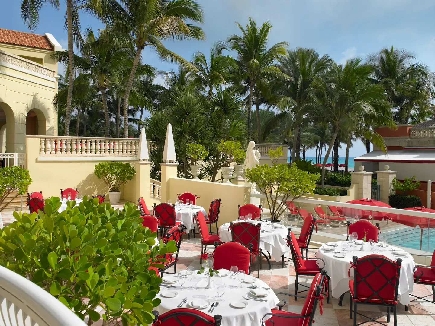 Outdoor dining at Il Mulino New York in Miami, with palm trees and red chairs.