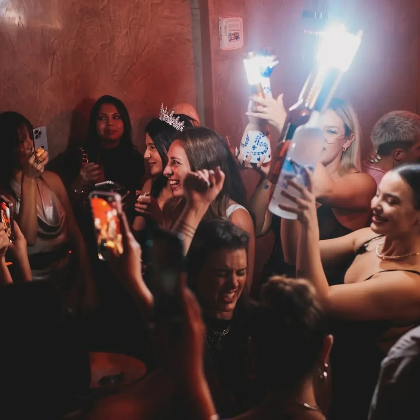 Party at La Otra nightclub in Miami, people celebrating with bottles and phones.