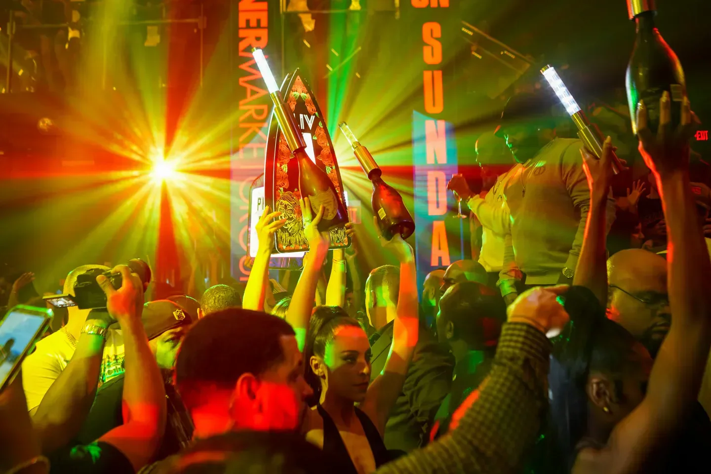 Energetic nightclub crowd at LIV Miami, with bottles raised and bright lights.