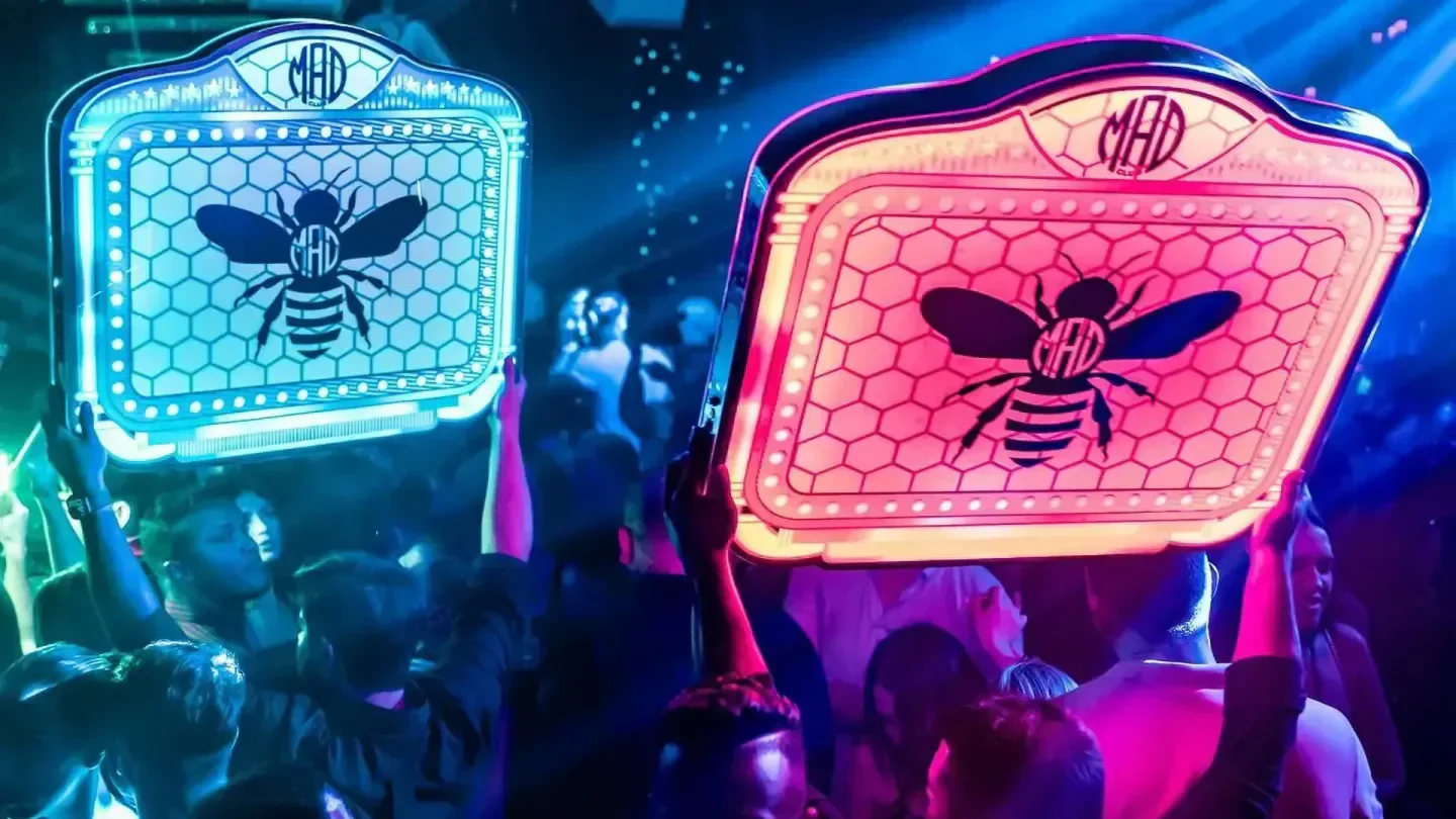 Energetic scene at MAD CLUB Wynwood in Miami, featuring vibrant illuminated bee signs.