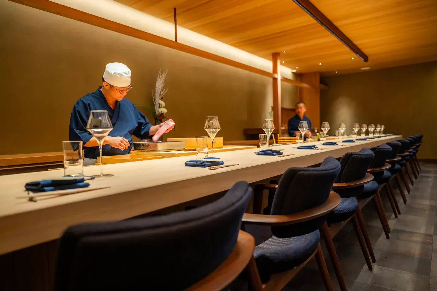 Chef preparing food at Shingo restaurant in Miami, with elegant dining area.