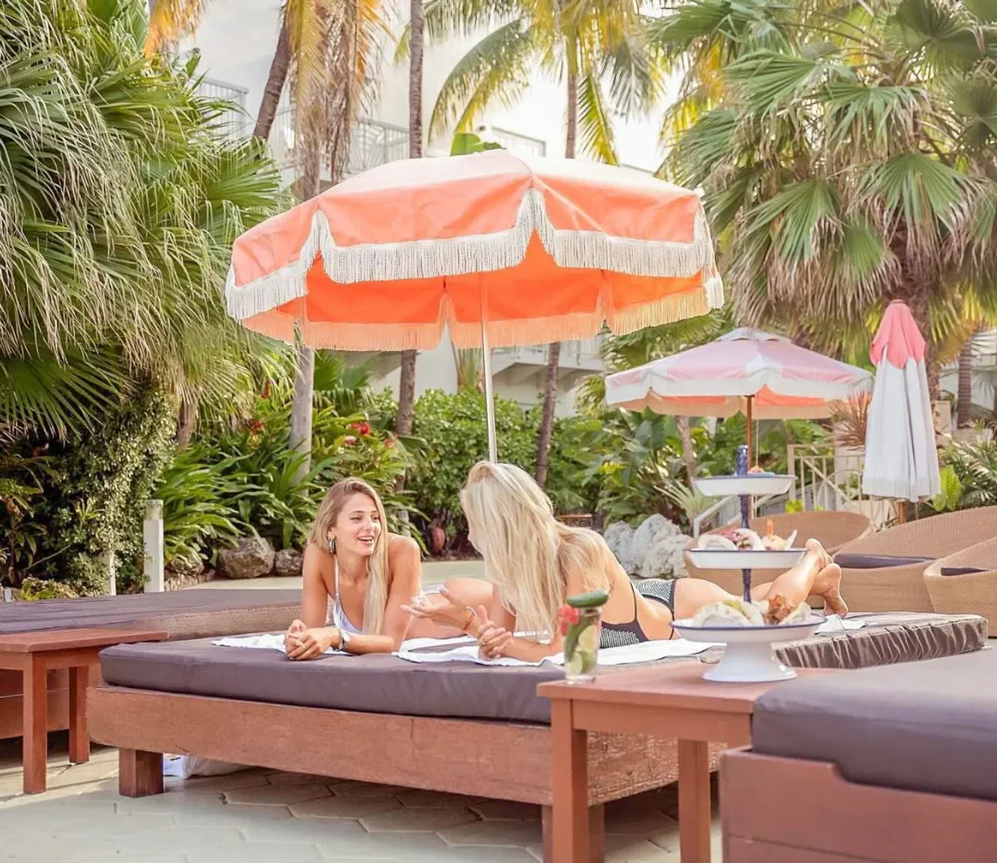 Two women relaxing at The Savoy Beach Club in Miami under a stylish parasol