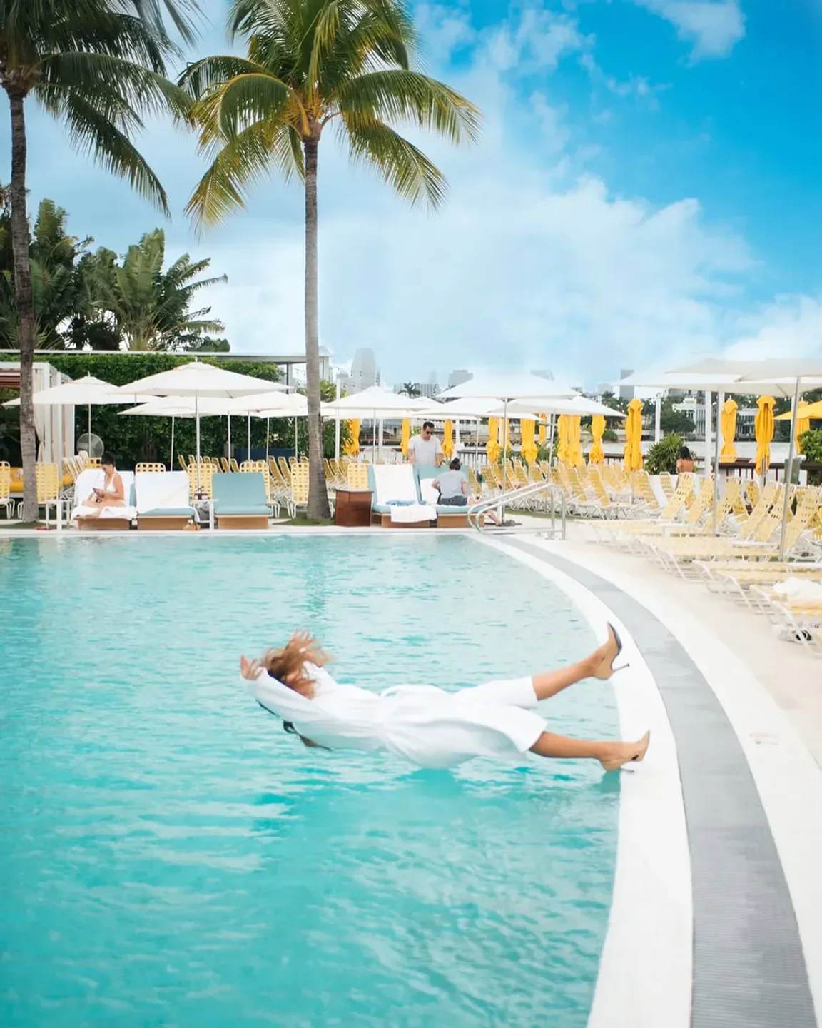 Woman diving into pool at The Standard Miami beach club with palm trees.